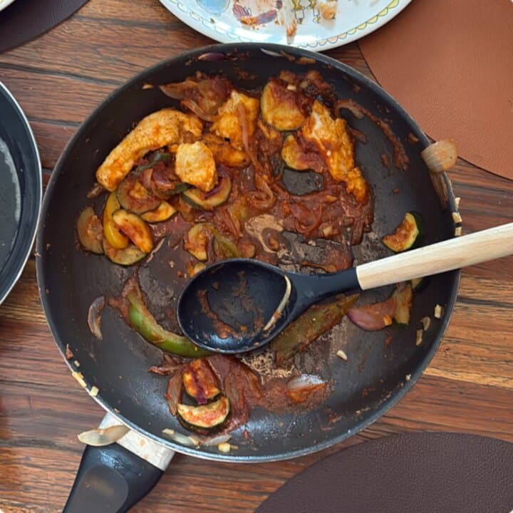 Een foto van een pan met restjes: kip, paprika, courgette en tomatensaus.